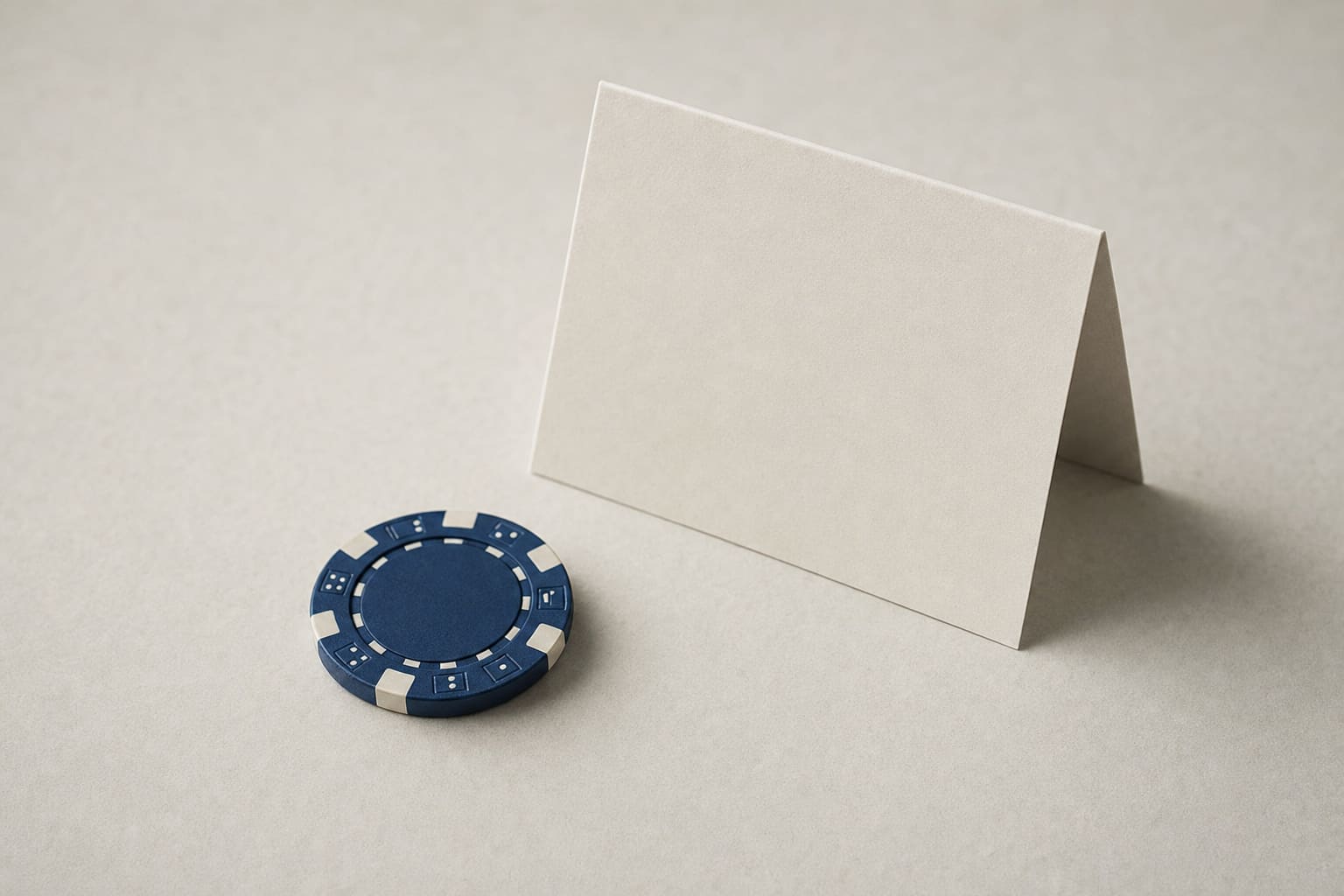 A single casino chip beside a plain folded card on a warm paper surface