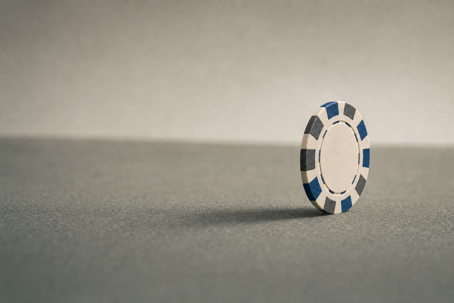 A single casino chip balanced on its edge on felt, with a soft long shadow